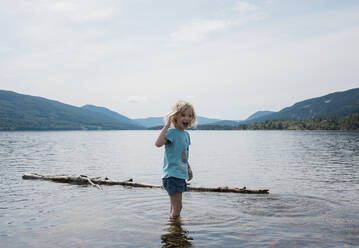 Young girl smiling standing in the water surrounded by mountains - CAVF63880