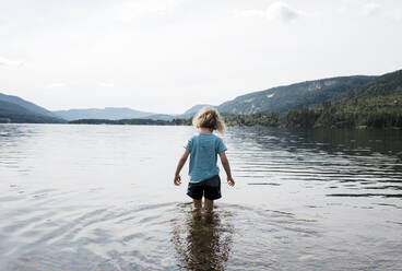 Young blonde girl walking in the sea with wet clothes by the mountains - CAVF63881