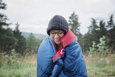 Porträt einer lächelnden Frau, eingewickelt in einen Schlafsack beim Wildcamping - CAVF63894