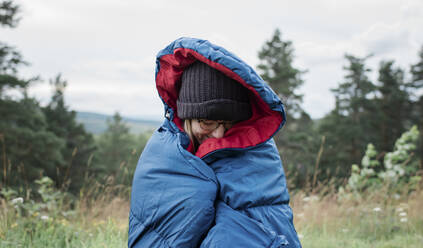 Porträt einer in einen Schlafsack eingewickelten Frau beim wilden Camping im Freien - CAVF63895