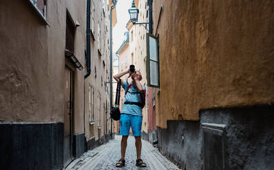 Älterer Mann, der mit einer DSLR Fotos von der Stadt macht, während er unterwegs ist - CAVF63911