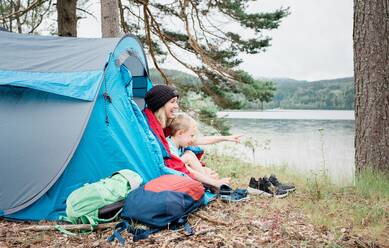 Mutter und Sohn sitzen lachend in einem Zelt beim Camping im Urlaub - CAVF63917
