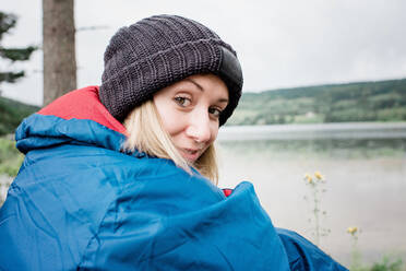 Porträt einer Frau mit Hut im Schlafsack beim Camping im Urlaub - CAVF63921