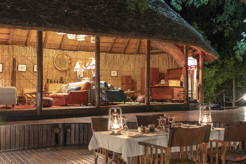 Nachts, ein gedeckter Tisch in einer luxuriösen Lodge, eine Lounge im Hintergrund - CAVF63951