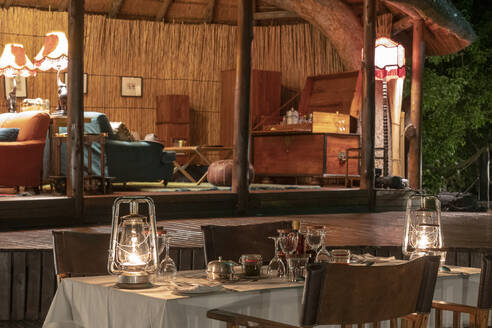 Nachts, ein gedeckter Tisch in einer luxuriösen Lodge, eine Lounge im Hintergrund - CAVF63952