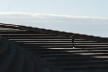Zurückgezogenes Bild einer Frau, die auf einer Treppe mit blauem Himmel im Hintergrund läuft - CAVF63976