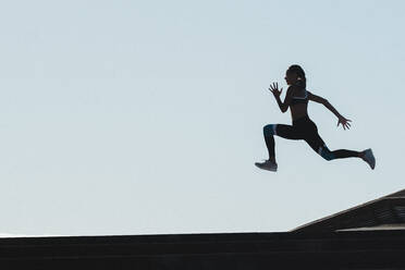 Silhouette einer springenden Sportlerin vor blauem Himmel - CAVF63978