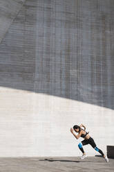 Gezogene Rückansicht einer Sportlerin, die auf einer vertikalen Betonfläche läuft - CAVF63984