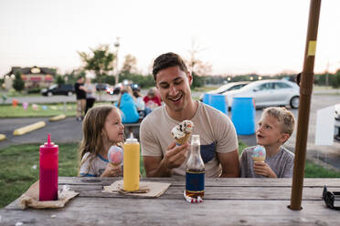 Junger Mann und Kinder essen Eis am Picknicktisch an einem Sommerabend - CAVF64022