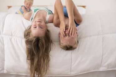 Schwester und Bruder lachen und spielen verkehrt herum auf dem Bett - CAVF64023