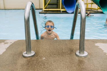 Aufgeregter Junge mit Schwimmbrille klettert die Leiter aus dem Pool - CAVF64027