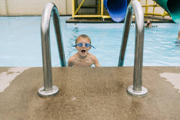 Excited boy with goggles climbs ladder out of pool - CAVF64027
