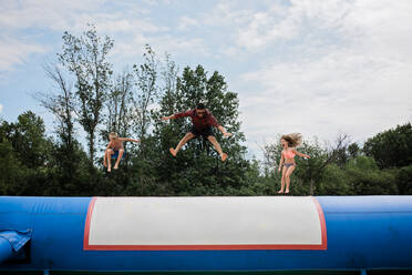 Junger erwachsener Mann und zwei Kinder springen an einem sonnigen Tag vor blauem Himmel - CAVF64029