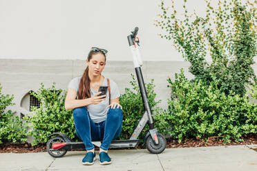 Frau schaut auf Telefon auf Scooter - CAVF64083