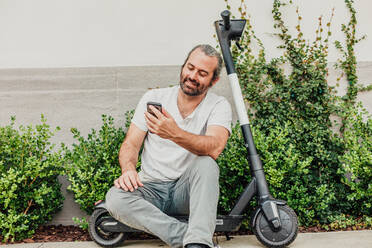 Man Sits on Scooter with Phone. - CAVF64084