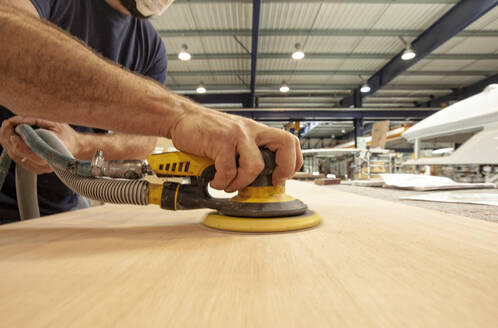 Schiffsbauer bei der Verwendung einer Schleifmaschine auf einem Holzbrett beim Bootsbau - CAVF64110