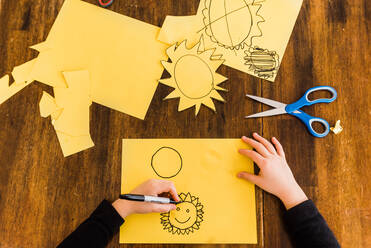 Young boy drawing and cutting out yellow sun - CAVF64164