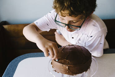 Ein kleiner Junge verziert seinen Schokoladen-Geburtstagskuchen mit Süßigkeiten. - CAVF64169