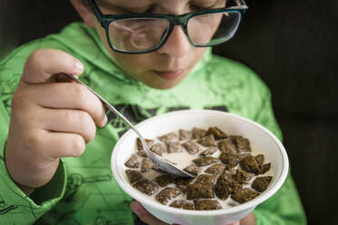 Ein Junge isst zum Frühstück sein Schokoladenmüsli aus einer weißen Schüssel. - CAVF64186