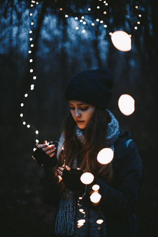 Young hipster woman holding Christmas lights while standing in park stock photo