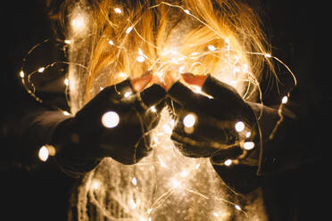 Close up woman holding Christmas lights outdoors in the dark - CAVF64258