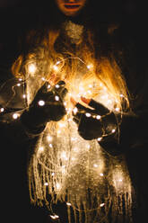Young woman holding Christmas lights outdoors in the dark - CAVF64260