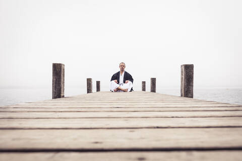 Man sitting on jetty doing yoga exercise, Lake Starnberg, Germany stock photo