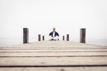 Mann sitzt auf Steg und macht Yoga-Übungen, Starnberger See, Deutschland - WFF00090