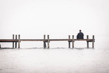 Rückenansicht eines Mannes, der auf einem Steg am Starnberger See sitzt, Deutschland - WFF00093