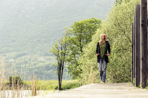 Young woman with red headphones walking on boardwalk at Lake Idro, Baitoni, Italy - WFF00101