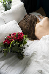 Bouquet of red roses on bed, sleeping woman on background - JOHF01957