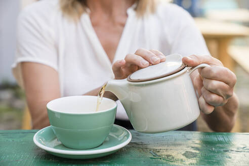 Frau gießt Tee in eine Tasse - JOHF01966