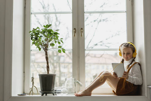 Girl sitting on windowsill with digital tablet - JOHF02010