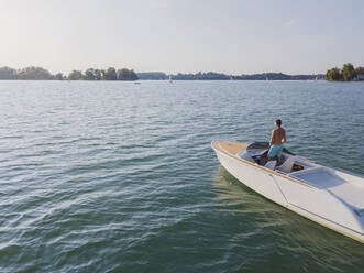 Germany, Bavaria, Shirtless man standing on motorboat floating in Chiemsee lake admiring distant landscape - MMAF01161