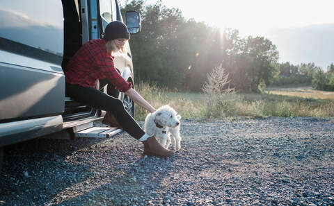 Woman sitting on a camper van stroking her dog whilst camping stock photo