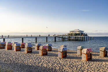 Germany, Schleswig-Holstein, Timmendorf, Strandkorb beach-chairs on sandy coastal beach with pier in background - EGBF00317