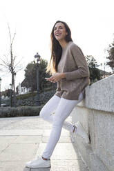 Laughing woman using her phone while leaning against a wall in Madrid - CAVF64407