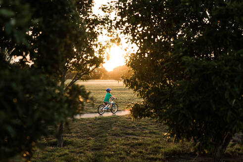 Vorschulkind fährt bei Sonnenuntergang mit dem Fahrrad auf dem Gehweg - CAVF64497