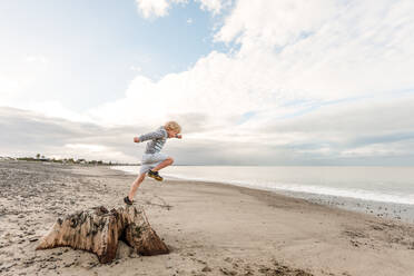 Junge springt von einem Baumstumpf am Strand - CAVF64498