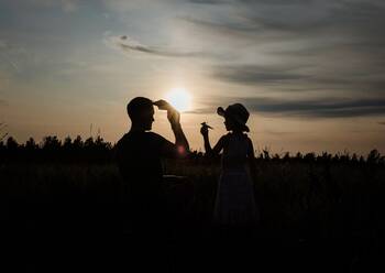Silhouette of father and daughter playing outside with paper aeroplane - CAVF64536