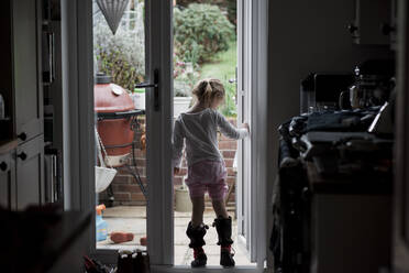 Young girl standing in a doorway whilst it rains outside in summer - CAVF64541