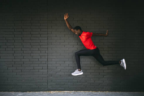 Young sportive man jumping in front of a brick wall - OCMF00759