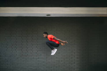 Young sportive man jumping in front of a brick wall - OCMF00764