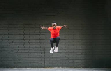 Young sportive man jumping in front of a brick wall - OCMF00770