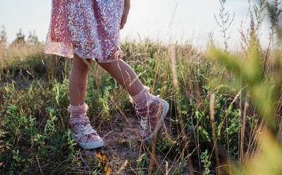 Young girls sparkly shoes and dress in the middle of a field at sunset - CAVF64590
