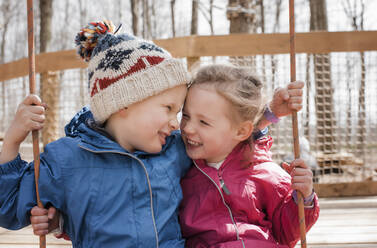 Mädchen und Junge auf einer Schaukel zusammen spielen und lachen draußen - CAVF64598