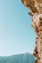 Pulled back view of male climber on wall with El Teide in the back - CAVF64611