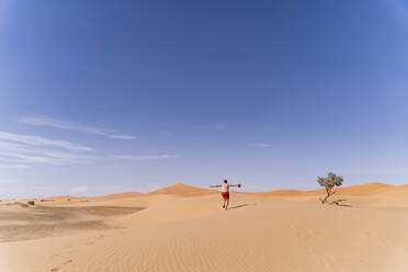 Overweight man with swimming shorts running in the desert of Morocco - OCMF00784