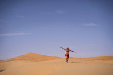 Overweight man with swimming shorts running in the desert of Morocco - OCMF00787