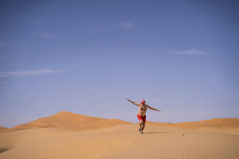 Übergewichtiger Mann in Badeshorts beim Laufen in der Wüste Marokkos - OCMF00787